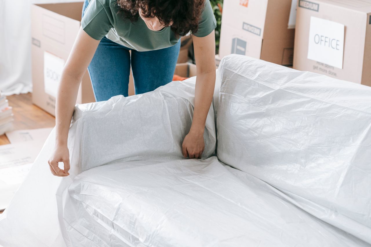 our-story Une femme enveloppe avec soin un canapé dans un matériau de protection tout en préparant des cartons dans une pièce lumineuse.
